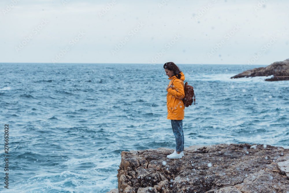 woman in yellow raincoat at the cliff enjoying sea view at stormy weather