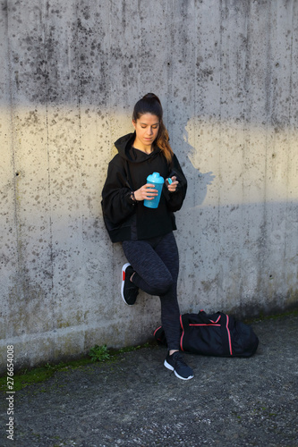 Sporty young woman on outdoor morning urban workout taking a rest for drinking water.