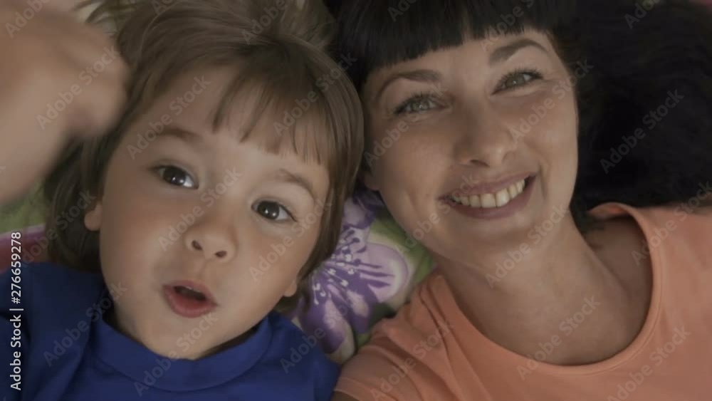 Family selfie. Excited young mother and child playing lying on bed and taking a selfie. Mother and son monkeying on camera and kissing. Portrait mom and baby. Family taking a selfie with a smartphone Family selfie. Excited young mother and child playing lying on bed and taking a selfie. Mother and son monkeying on camera and kissing. Portrait mom and baby. Family taking a selfie with a smartphone