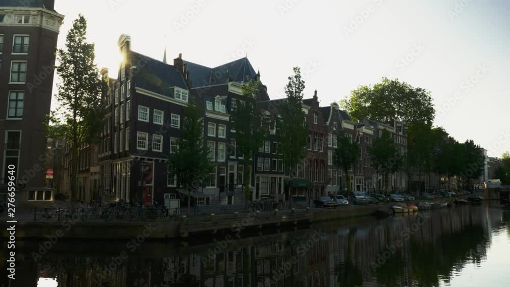 Beautiful early morning sunlight in a beautiful Amsterdam neighborhood. A calm canal has a reflection of the old architecture homes lining the street. Beautiful early morning sunlight in a beautiful Amsterdam neighborhood. A calm canal has a reflection of the old architecture homes lining the street.
