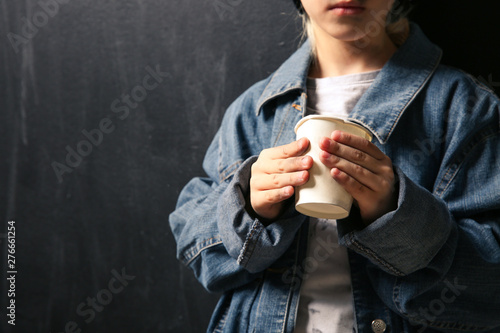 Homeless little girl with cup on dark background photo