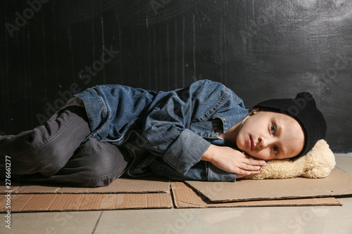 Homeless little girl lying on floor near dark wall