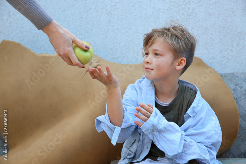 Woman giving food to homeless little boy outdoors photo