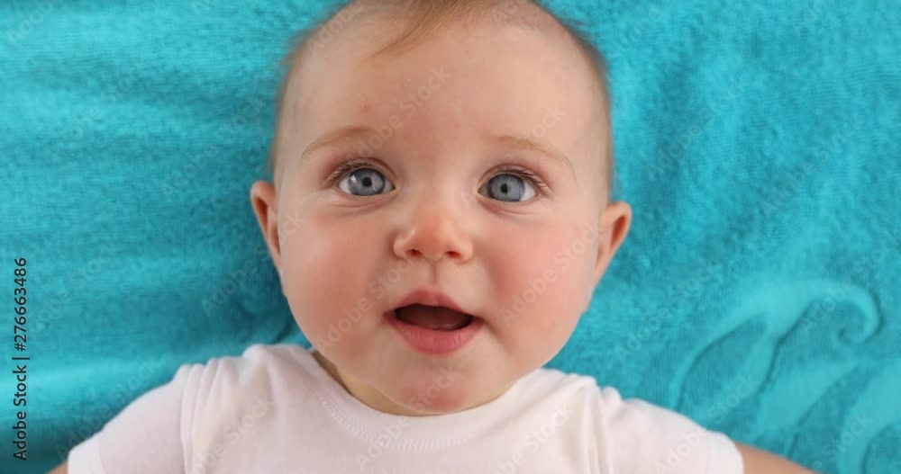 Adorable blue eyed baby with opened mouth lying on blue towel and looking at camera Adorable blue eyed baby with opened mouth lying on blue towel and looking at camera