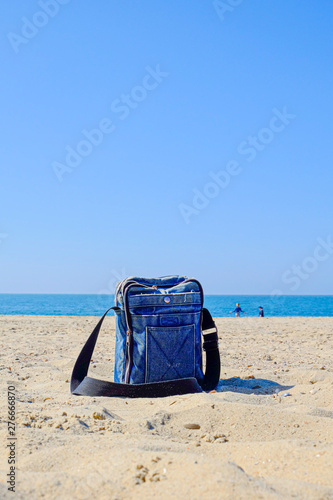 Close-up of blue denim bag with black strap on sandy beach against blue sky