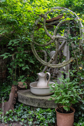 überwuchertes Brunnenrad in einem Garten mit Keramikgefäßen