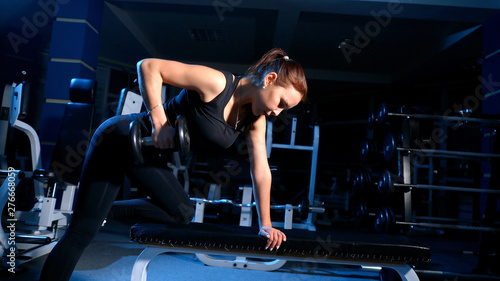 A girl performs a dumbbell with one hand in the slope using a bench. exercise on the broadest back muscles with dumbbells. © cinematri