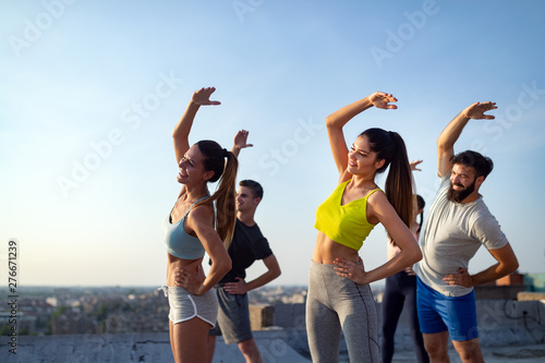 Group of young happy people friends exercising outdoors at sunset.