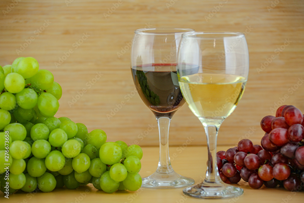 Red and white wine with green and red grapes on a wooden table with a wooden wall
