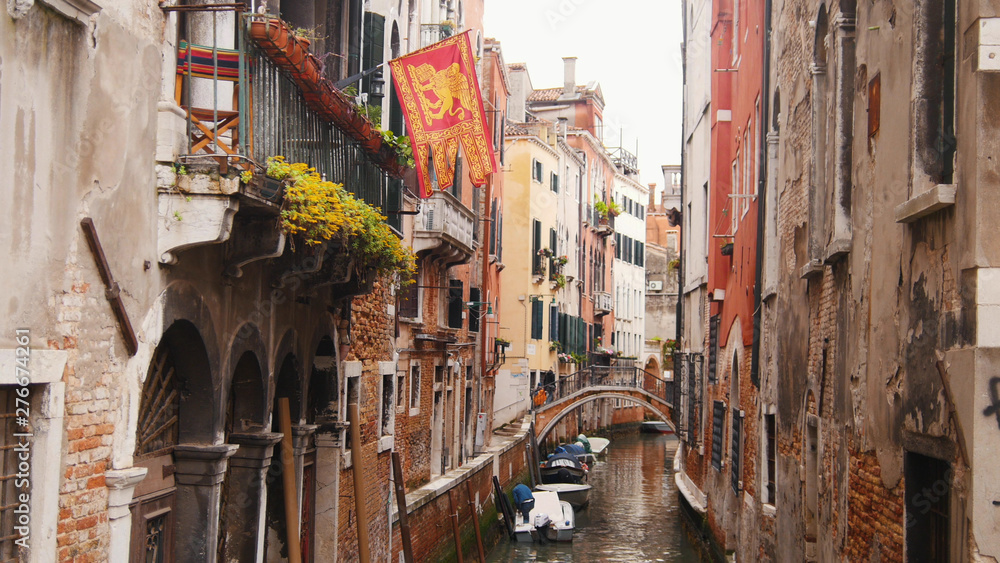 Narrow streets of Venice - canal filled with water - moored boats - flag if Venice