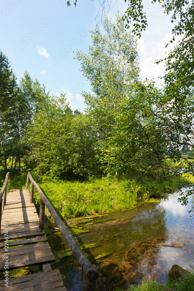 Summer landscape with an old wooden bridge over an overgrown river on the edge of the forest on a sunny day. Summer travel and hiking in the forest Summer landscape with an old wooden bridge over an overgrown river on the edge of the forest on a sunny day. Summer travel and hiking in the forest