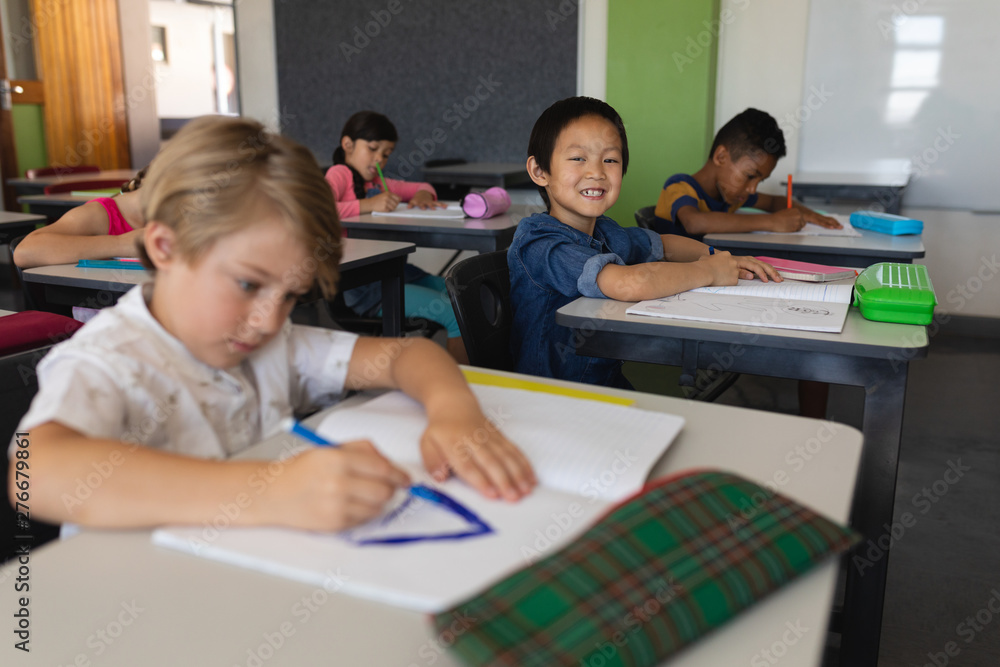 Schoolboy looking at camera while studying in classroom Schoolboy looking at camera while studying in classroom