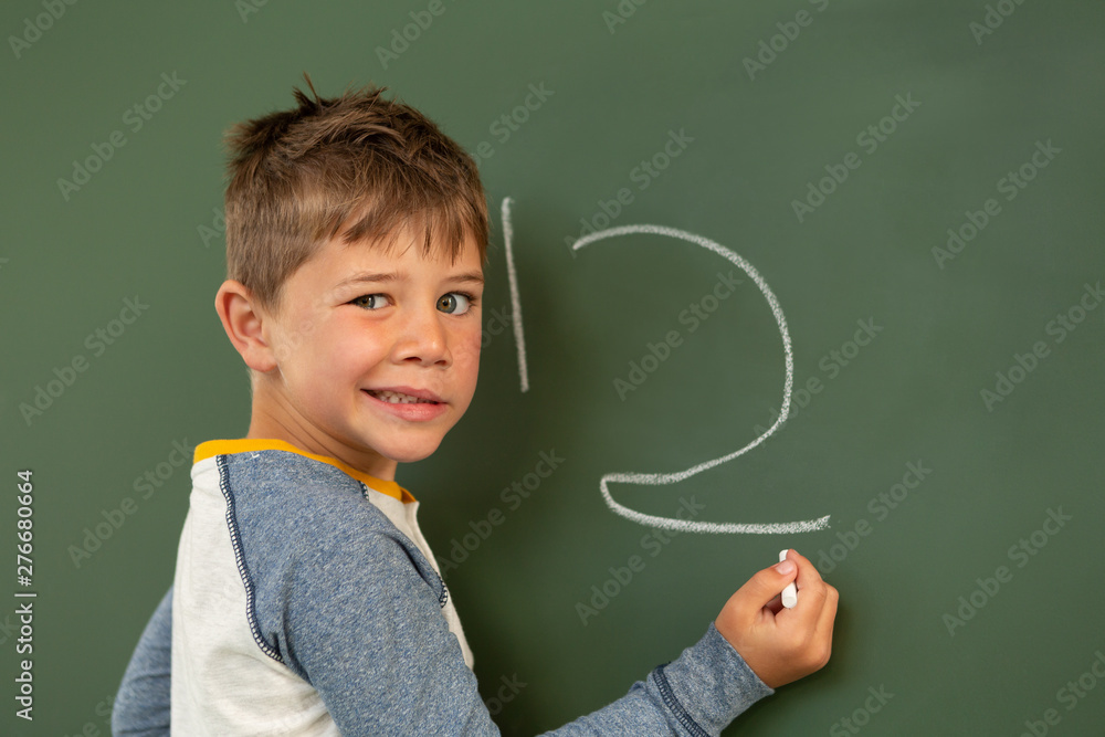 Schoolboy doing math on green chalkboard in a classroom