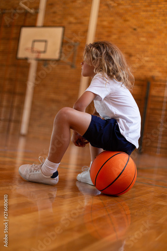 Schoolgirl sitting on basketball on basketball court