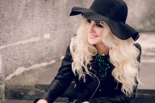 The girl in the black hat and leather jacket sits and smiles © ribalka yuli