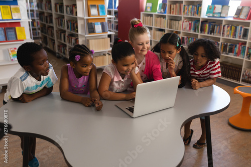 Schoolkids studying together on laptop at table in school library