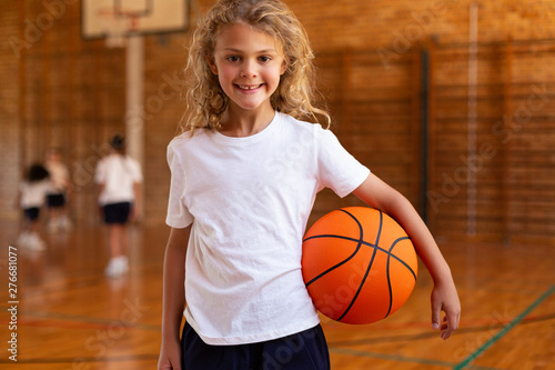 Schoolgirl with basketball looking at camera in basketball court