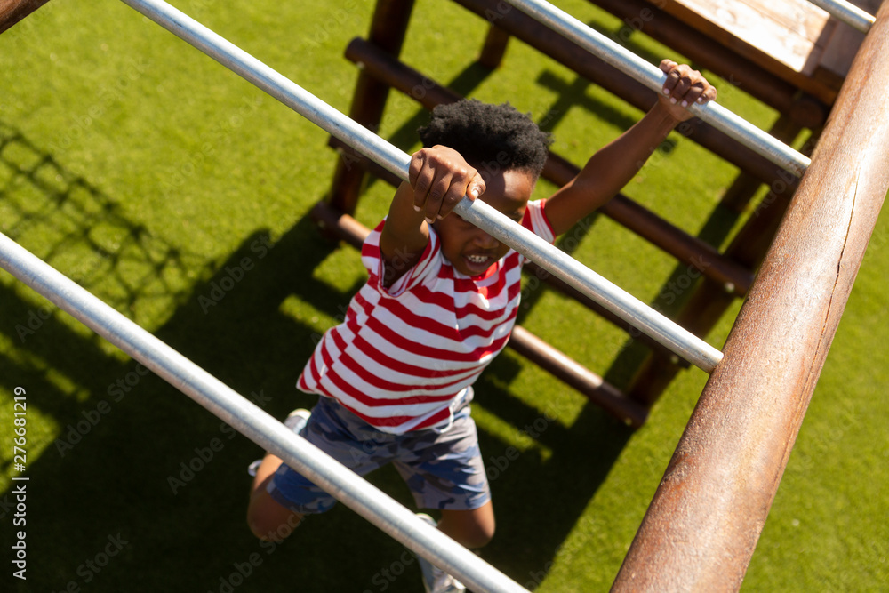 Fototapeta premium Schoolboy playing on horizontal ladder in the school playground