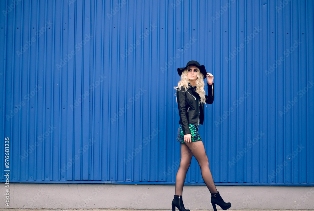The girl in the black hat and leather jacket goes along the blue wall The girl in the black hat and leather jacket goes along the blue wall