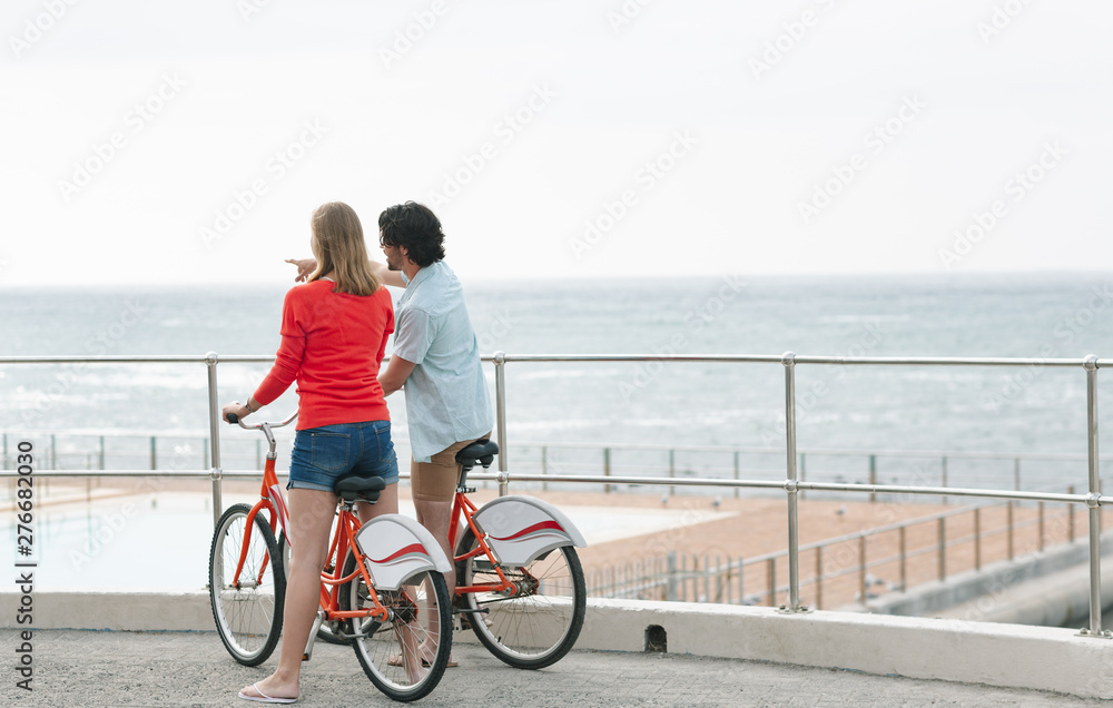 Caucasian couple interacting with each other while holding bicycle at promenade
