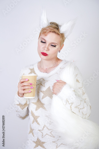 pretty plus size caucasian woman wearng fashion knitted warm sweater and fur cat ears and posing on white studio background alone with cup of milk photo