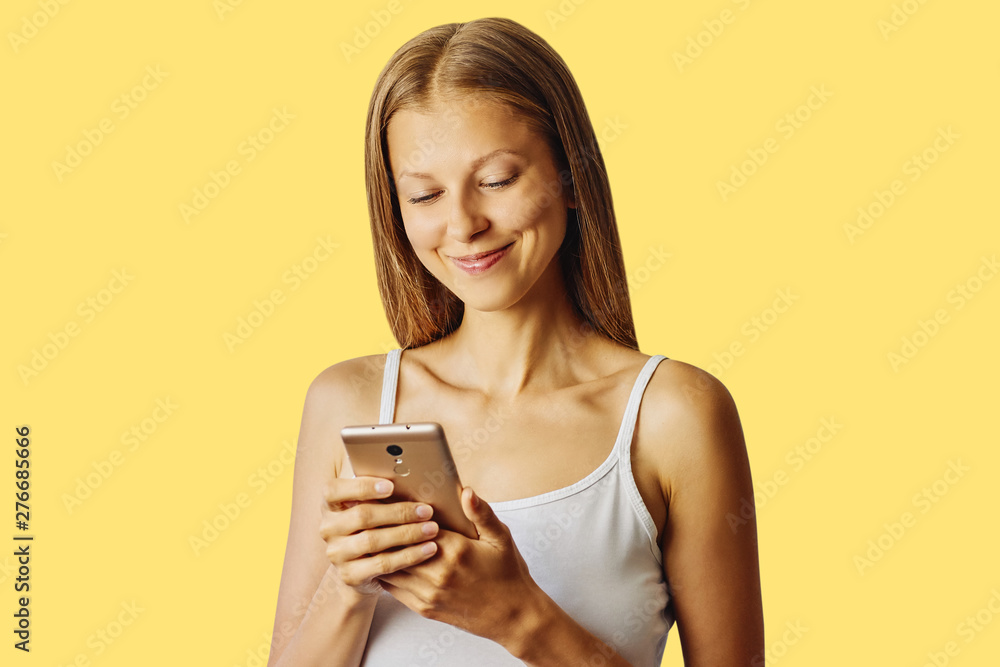 Happy smiling woman holds her cellphone, isolated over yellow background Happy smiling woman holds her cellphone, isolated over yellow background