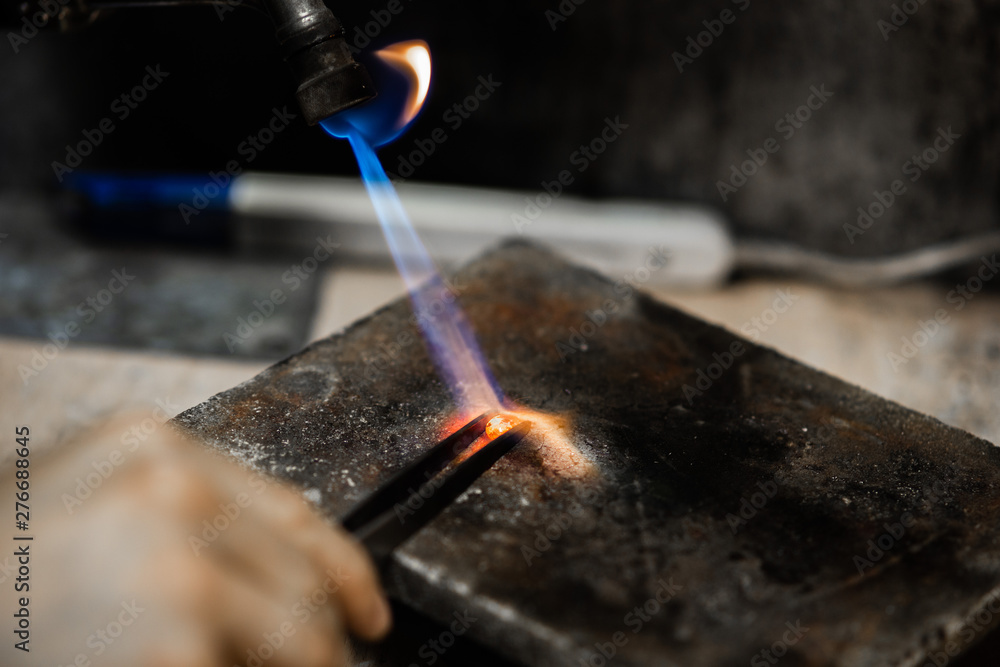 Craft jewelry with a torch flame against a dark background. Jeweler handles  metal rail by heating it.Beautiful bright close up photo. Stock Photo