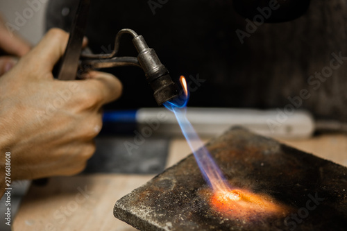 Craft jewelry with a torch flame against a dark background. Jeweler handles metal rail by heating it.Beautiful bright close up photo.