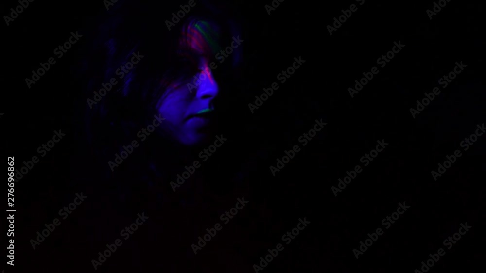 Close-up portrait of lovely confident girl with stage neon make-up going to make perfomance. Fashion model on black background. Night club, party, psychedelic concepts. Slow motion. Close-up portrait of lovely confident girl with stage neon make-up going to make perfomance. Fashion model on black background. Night club, party, psychedelic concepts. Slow motion.