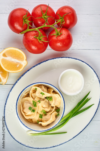 dumplings with parsley and onion at white wooden table top. Pelmeni - traditional russian cuisine dish dough with minced meat inside. decorated with tomatoes