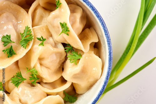 dumplings with parsley and onion at white wooden table top. Pelmeni - traditional russian cuisine dish dough with minced meat inside. close up