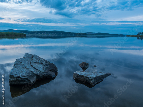 Calm, serenity, meditation concept. Sunset on the lake, stones in the water in the foreground, quiet water, cloudless sky. Blue hour