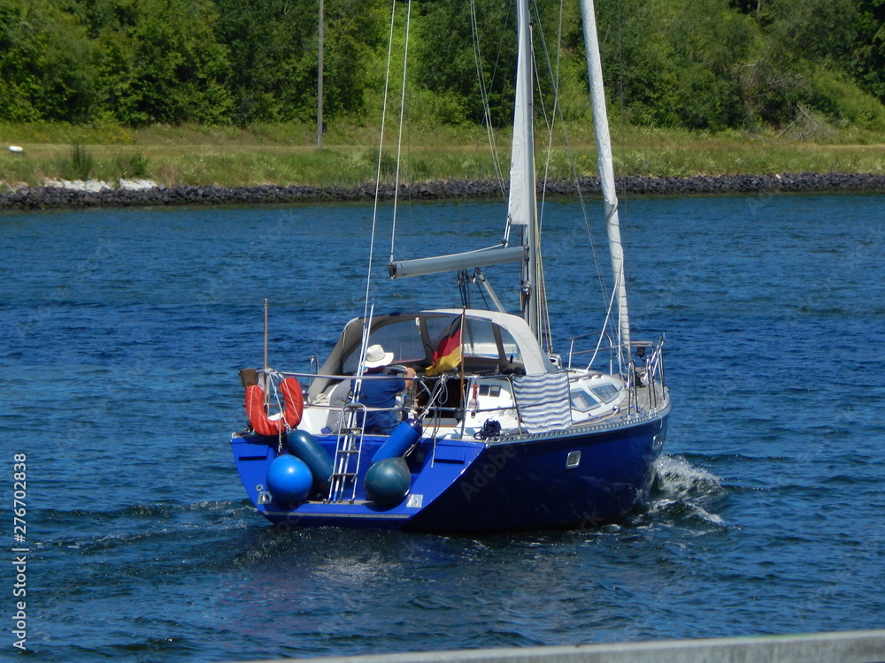 Obraz premium Skipper with sailing boat on a blue river, sailing trip on the Kiel Canal