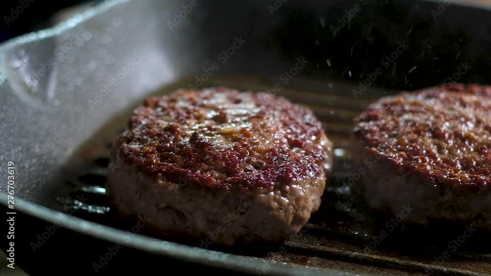 two meat fat juicy burgers with a hard crispy brown crust are fried on a hot frying pan with a non-stick grill. Boiling oil splashes heavily. Panoramic slow motion picture of the Cooking process in th two meat fat juicy burgers with a hard crispy brown crust are fried on a hot frying pan with a non-stick grill. Boiling oil splashes heavily. Panoramic slow motion picture of the Cooking process in th