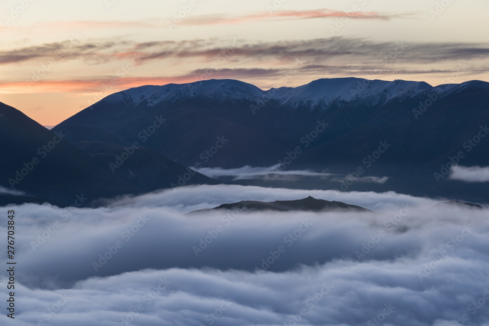 The valley is flooded in mist in a mountain environment. Over the fogs, only the high peaks of the mountains rise beneath the sunny sky. Misty morning. Beuatiful landscape concept.