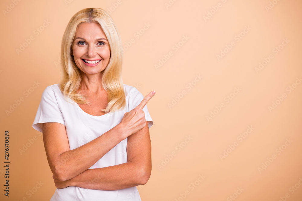 Photo of middle age lady hand indicate empty space advising new product wear white casual t-shirt isolated pastel beige background Photo of middle age lady hand indicate empty space advising new product wear white casual t-shirt isolated pastel beige background