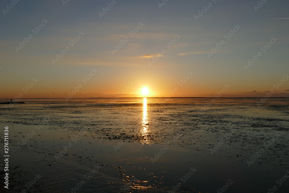 Sunset on the North Sea directly on the beach. Orange sky and low tide.