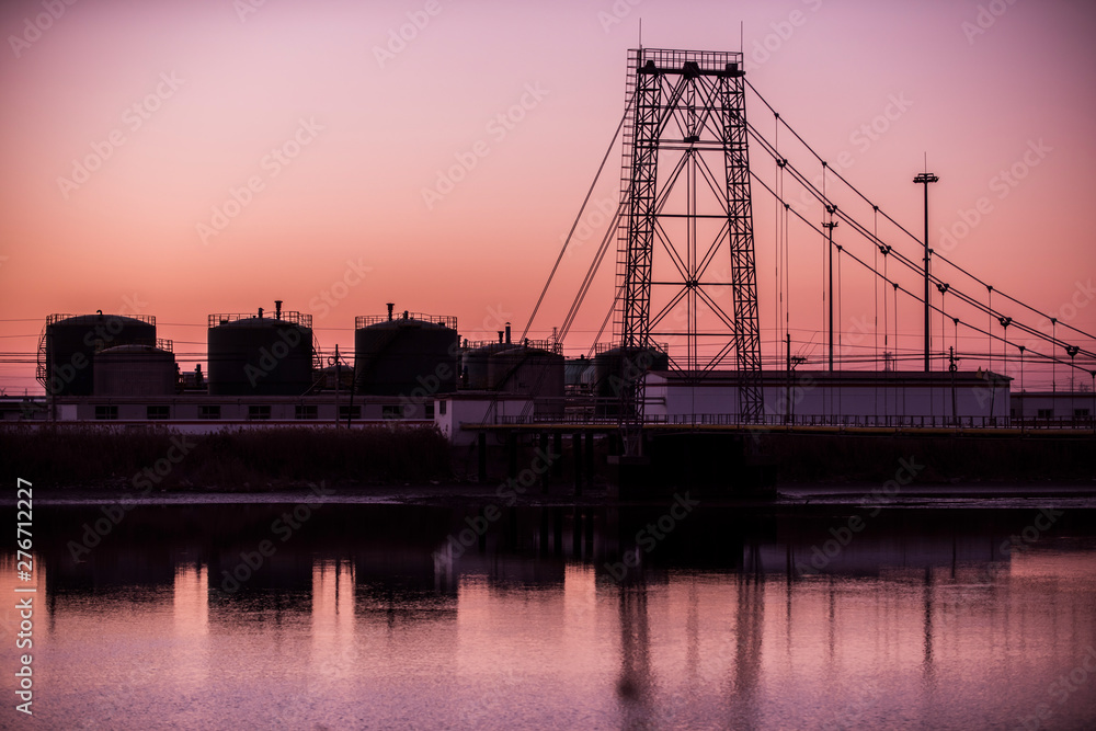 Obraz premium Silhouetted against the setting sun, the exterior of an oil refinery by the sea