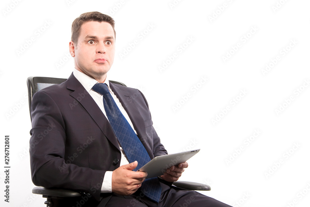 Surprised man in a suit with a tablet in his hands sitting in a chair on a white background in the studio. Surprised man in a suit with a tablet in his hands sitting in a chair on a white background in the studio.