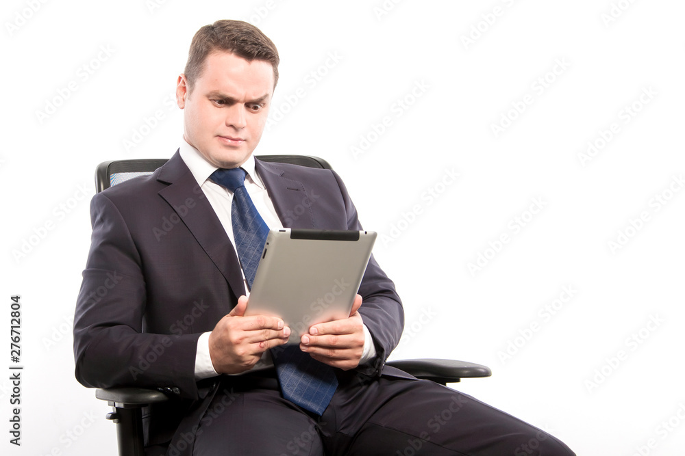 Businessman in surprise looks into the tablet while sitting in a chair on a white background in the studio. Businessman in surprise looks into the tablet while sitting in a chair on a white background in the studio.