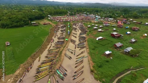 Wide high angle  dolly shot of Nampan village market with its blue, green and brown decorated roof-tops, village homesteads, and docked boats at Inle lake channel, Shan State, Myanmar photo