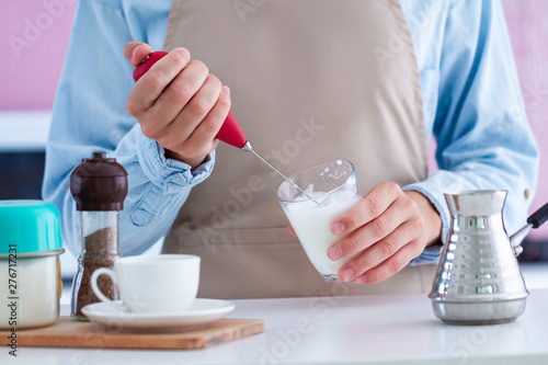 Woman in apron making coffee with using a milk frother at kitchen at home photo
