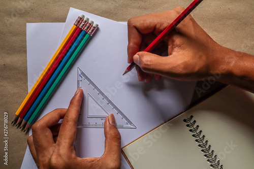 The hands of people who are using pencils and rulers and educational equipment, written on white paper, brown background.