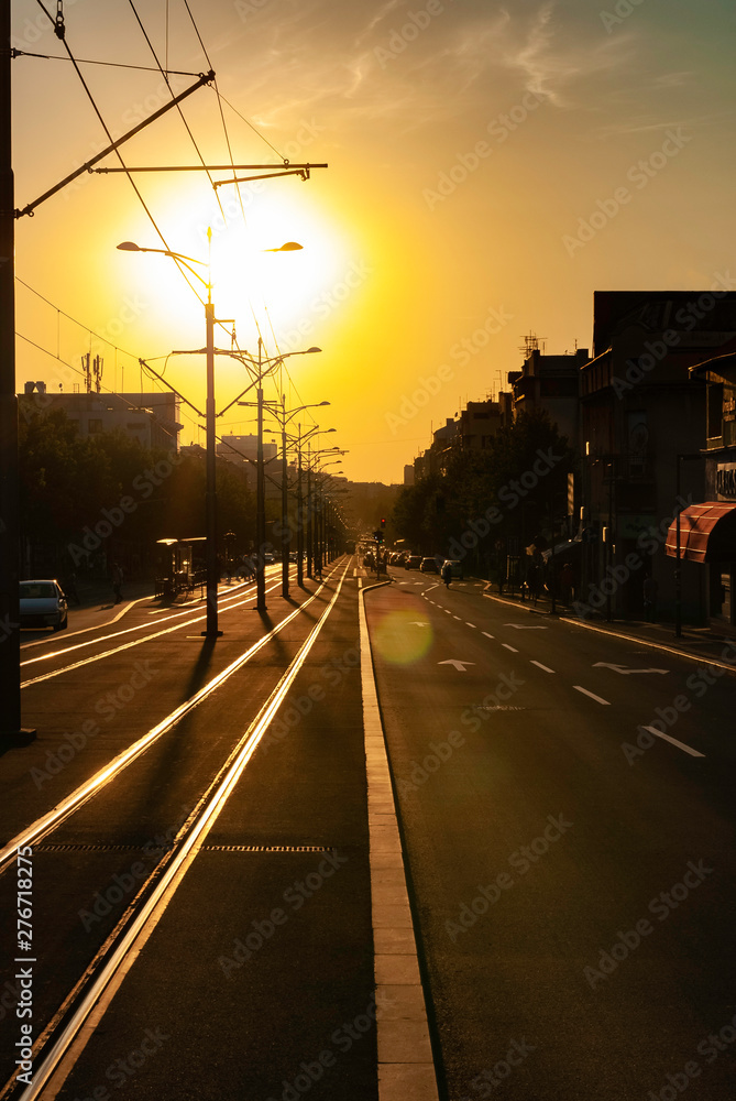 Urban city sunset vertical image of city street boulevard direct sunlight lens flare tram track tramway rails empty street trolleycar path