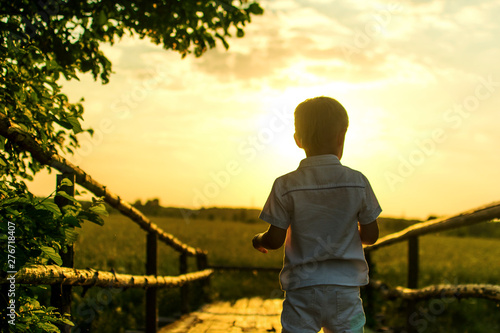 boy plays on an old wooden bridge on a bright warm evening at sunset
