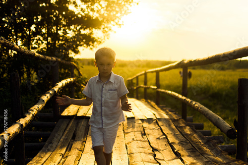 boy plays on an old wooden bridge on a bright warm evening at sunset