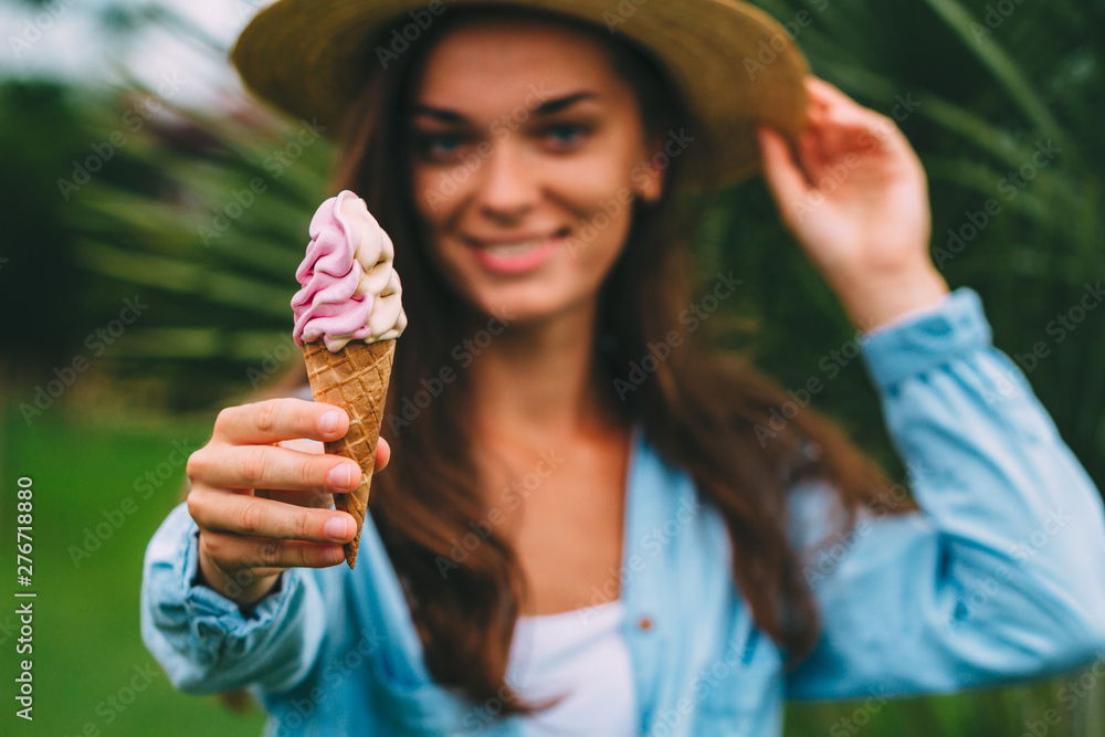 Happy cheerful hipster woman in shirt and hat eating sweet ice cream outdoors in hot summer day