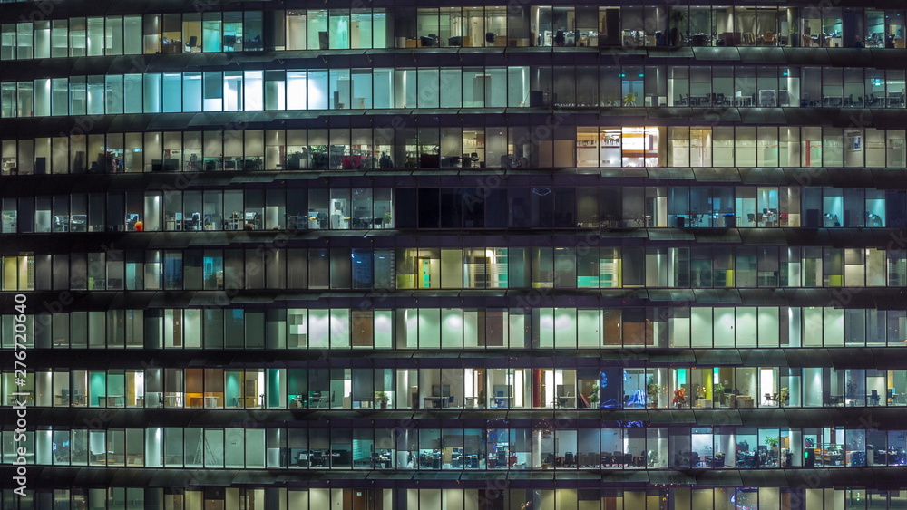 Working evening in glass office building with numerous offices with glass walls and windows timelapse