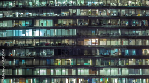 Working evening in glass office building with numerous offices with glass walls and windows timelapse