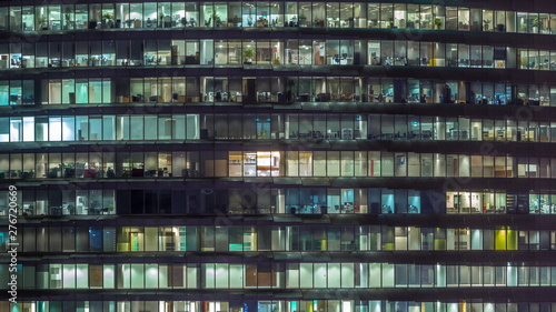 Working evening in glass office building with numerous offices with glass walls and windows timelapse